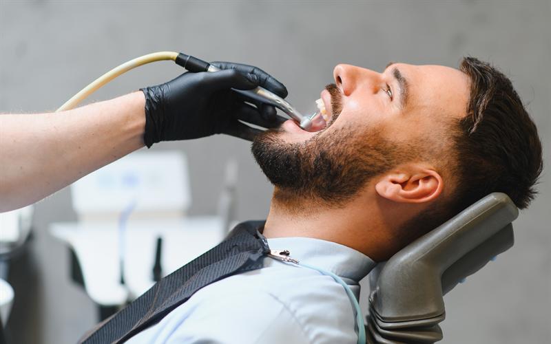 Un paciente recostado en el sillón mientras el dentista trabaja en su boca.