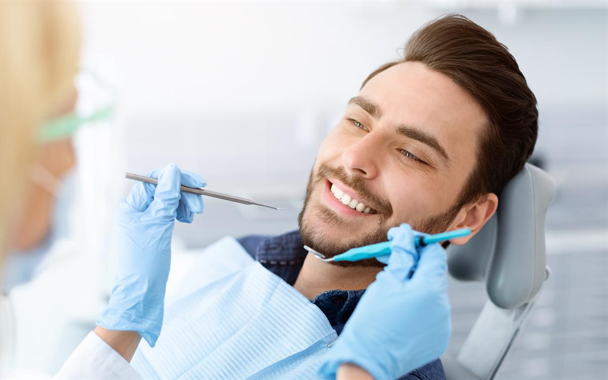 Un paciente sonríe recostado en el sillón mientras la dentista se acerca con el instrumental.