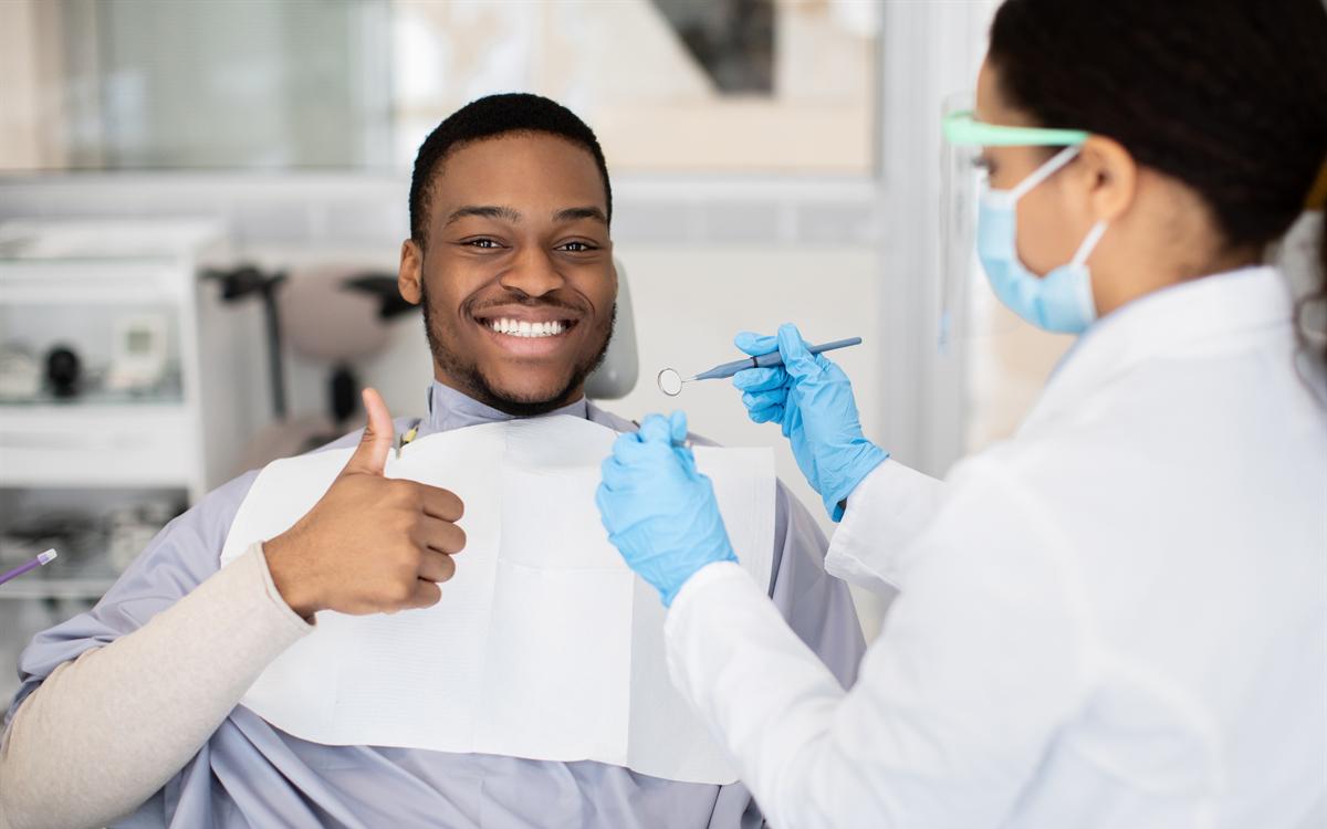 Un paciente levanta el pulgar, sonriendo, junto a la dentista que sostiene el espejo bucal.